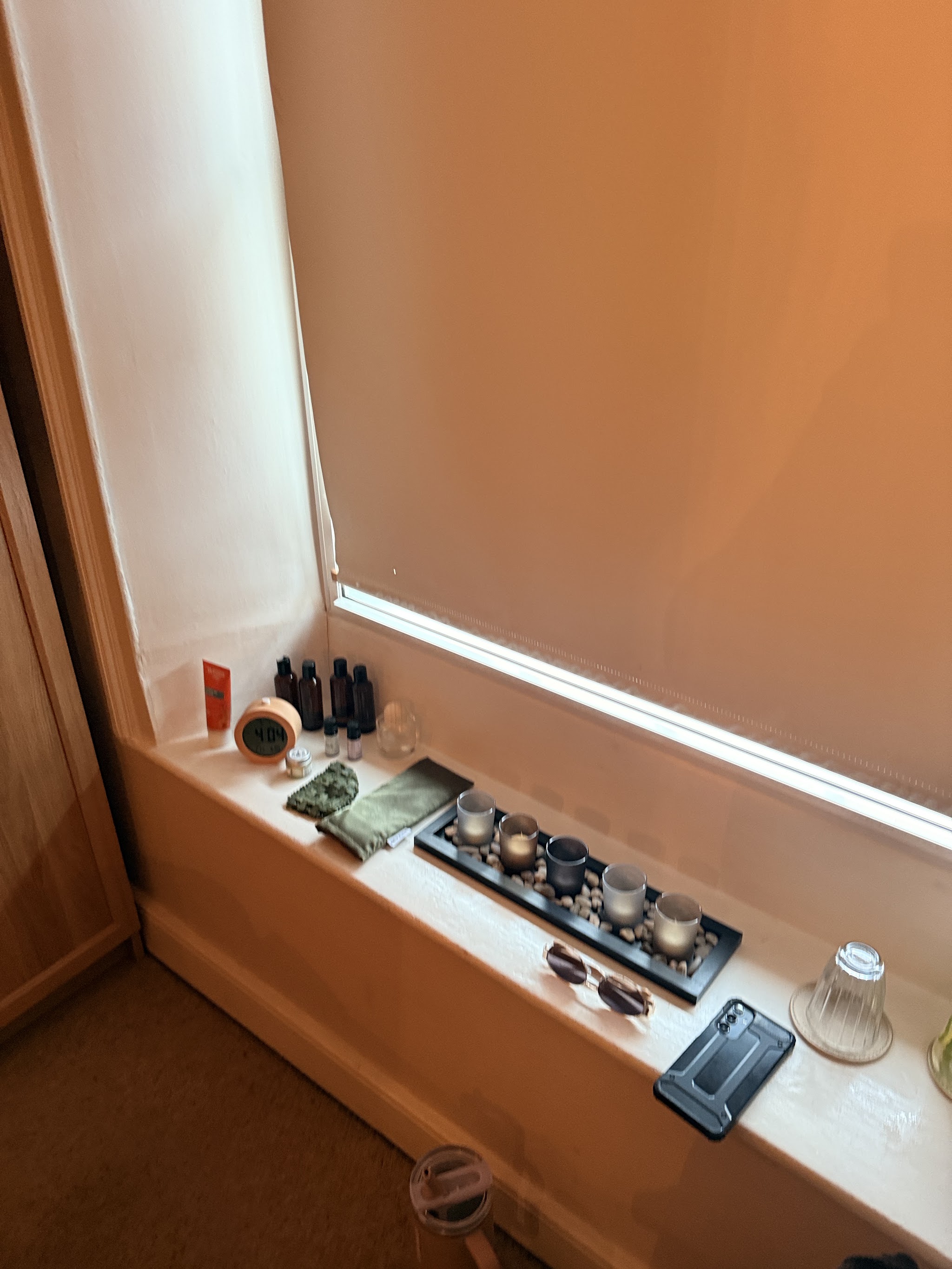 Oils, a tea-light tray and an eye pillow along the treatment room window sill in warm light